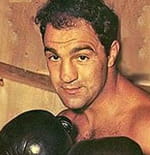 Primer plano del boxeador Rocky Marciano con guantes negros y en posición de combate.