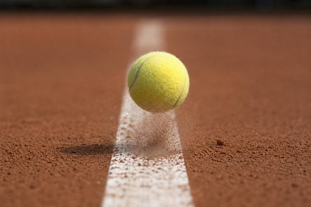 Pelota de tenis botando sobre la línea de una pista de tierra batida